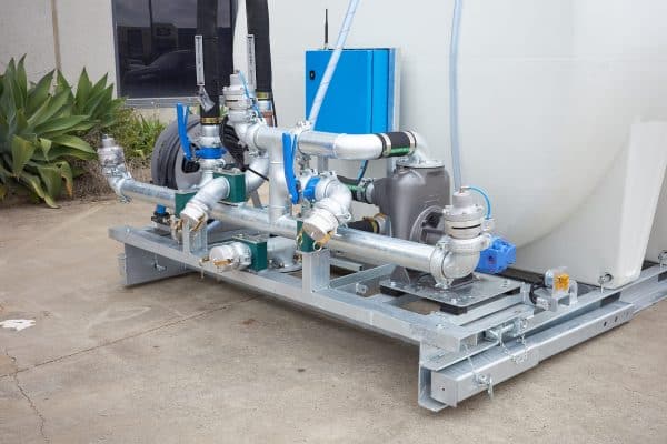 The 8000L Civmaster Premium Hydraulic Water Cart features pipes, valves, and gauges on a metal frame, positioned outdoors near a building and greenery.