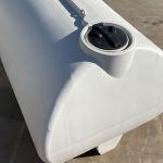 A large, white, horizontal plastic storage tank by National Water Carts with a black circular lid sits on a concrete surface. Shadows indicate it is outdoors in bright sunlight.