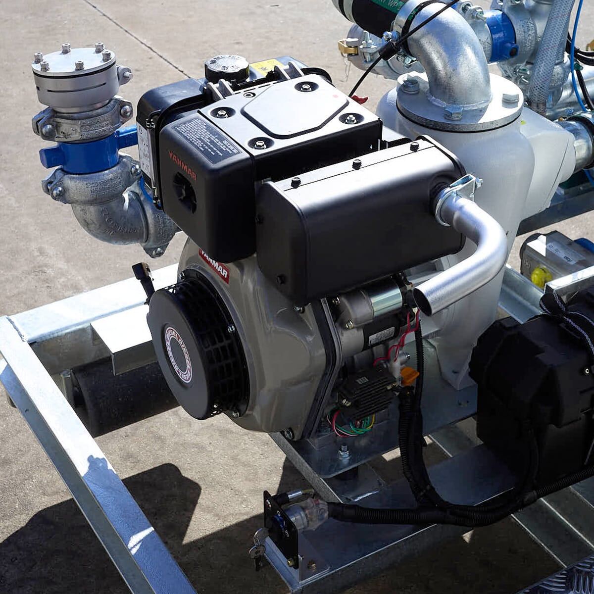 A close-up of a Yanmar L100N diesel engine and pipe manifold mounted on a slip-on water cart frame.