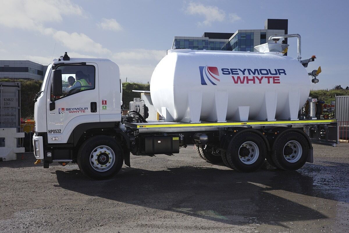 A white Seymour Whyte water truck truck is parked on a construction site, with building and construction materials visible in the background.