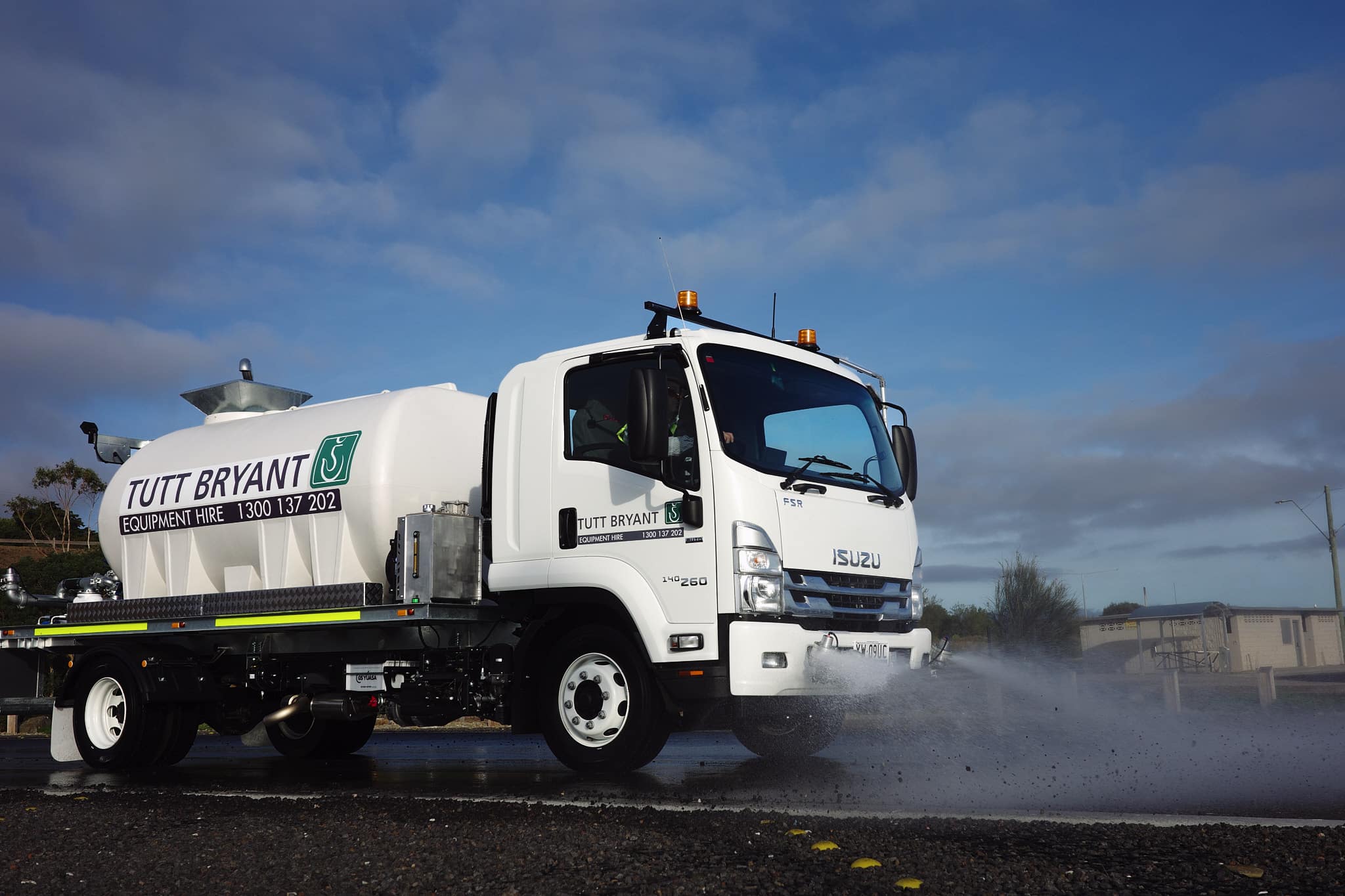 An 8,000-litre CivMaster FSR hydraulic water truck with Tutt Bryant Equipment Hire branding sprays water onto the road surface.
