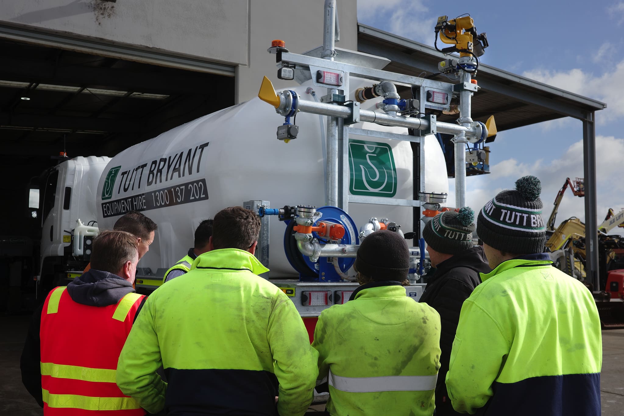 Tutt Bryant workshop team members in high-visibility PPE stand in front of a CivMaster EXM FVZ CANbus water truck during a site induction at the Tutt Bryant facility in Moolap.