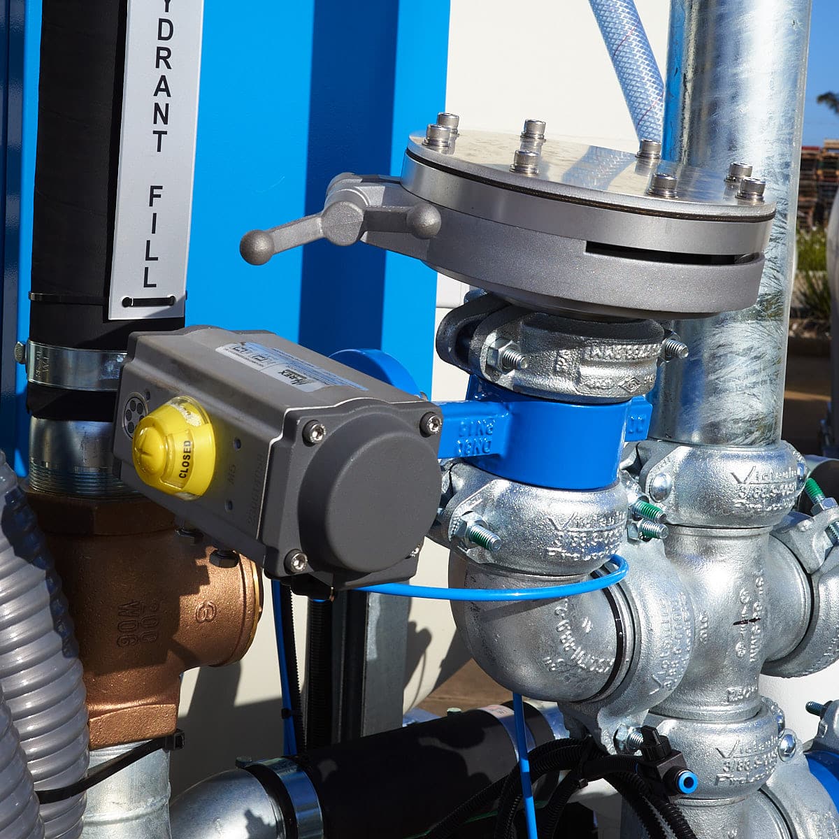 A close-up of an actuated butterfly valve connected to a spray head on a slip-on water cart pipe manifold.