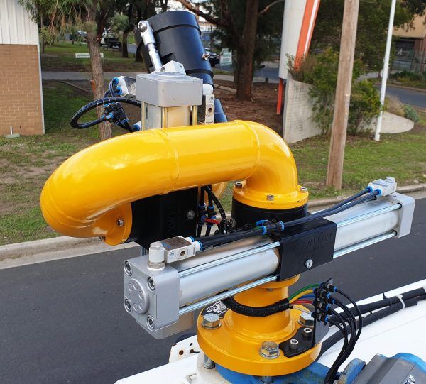 A close-up of the E360XD Extreme Duty Electric Water Cannon, featuring a bright yellow industrial robotic arm with sensors and wires, is mounted outdoors on a platform near a street and buildings by National Water Carts.