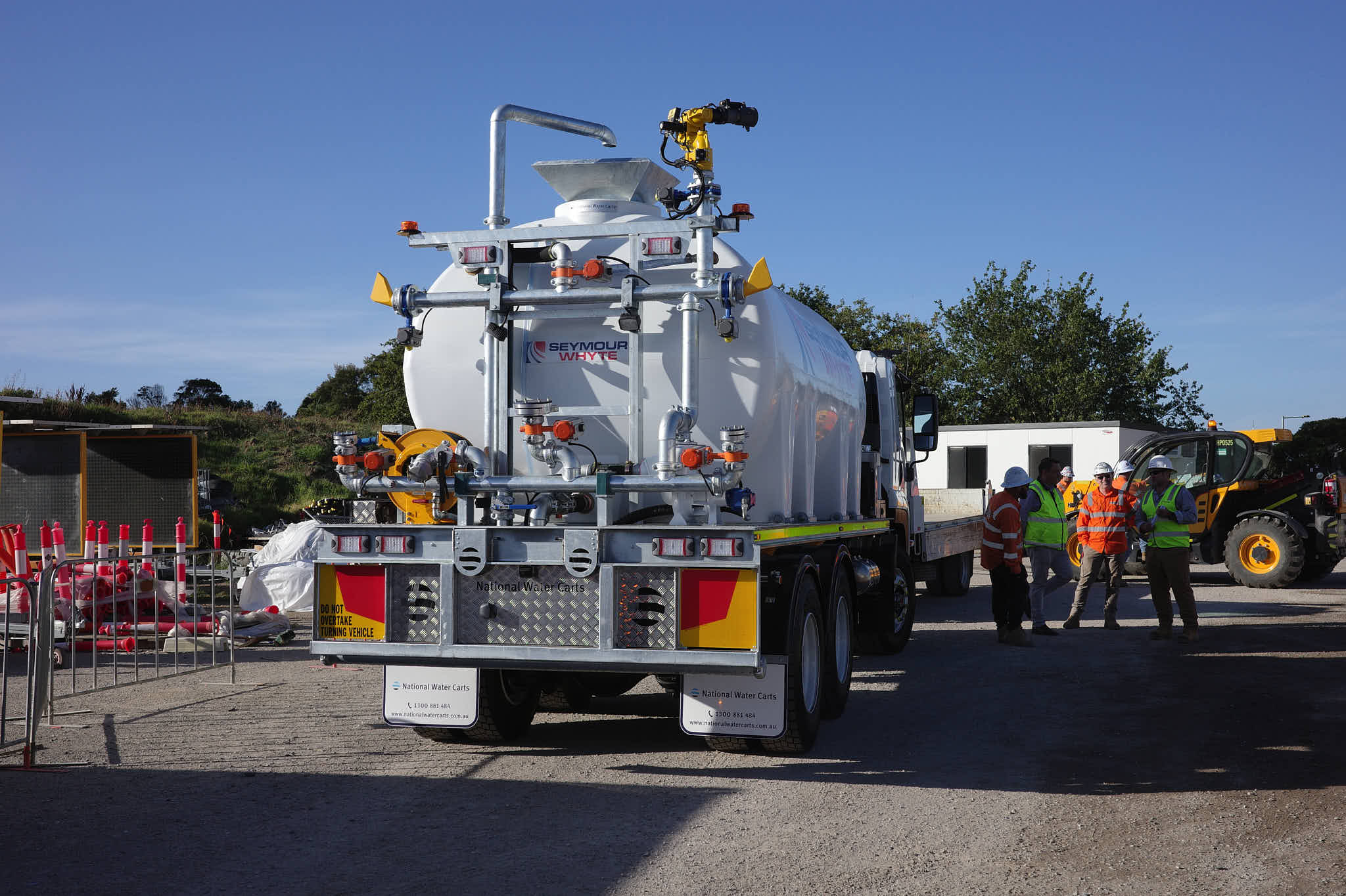An Isuzu FVZ CivMaster EXM CANbus hydraulic water truck on a construction site, with workers in high-visibility PPE and site equipment in the background.